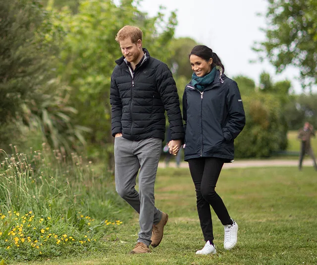 Couple walking hand in hand through a park, both wearing jackets.