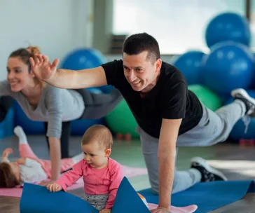 Adults with babies doing yoga exercises on mats in a gym with blue exercise balls.