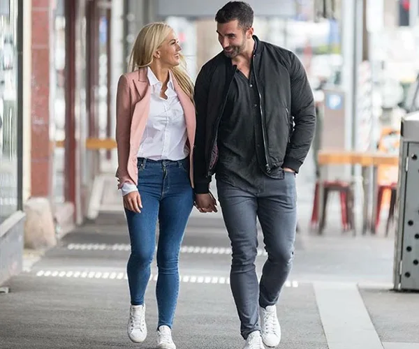 A couple walks hand-in-hand down a city street, both smiling and dressed casually.