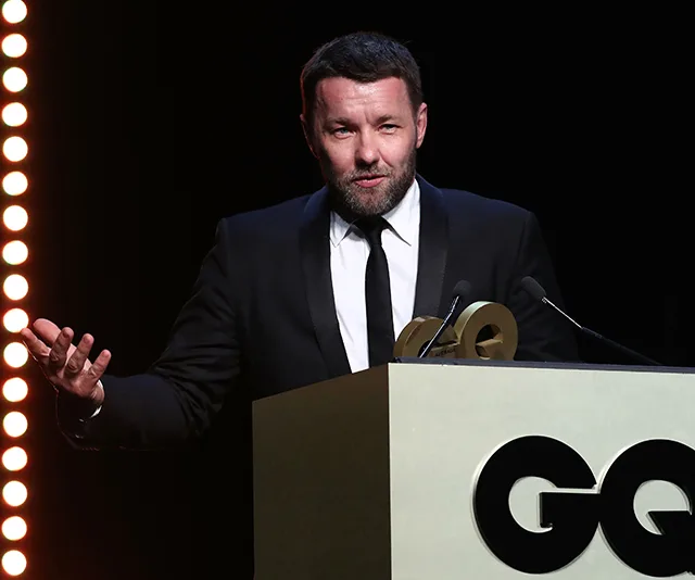 Man in a suit speaks at a podium with a "GQ" logo, stage lights in the background.