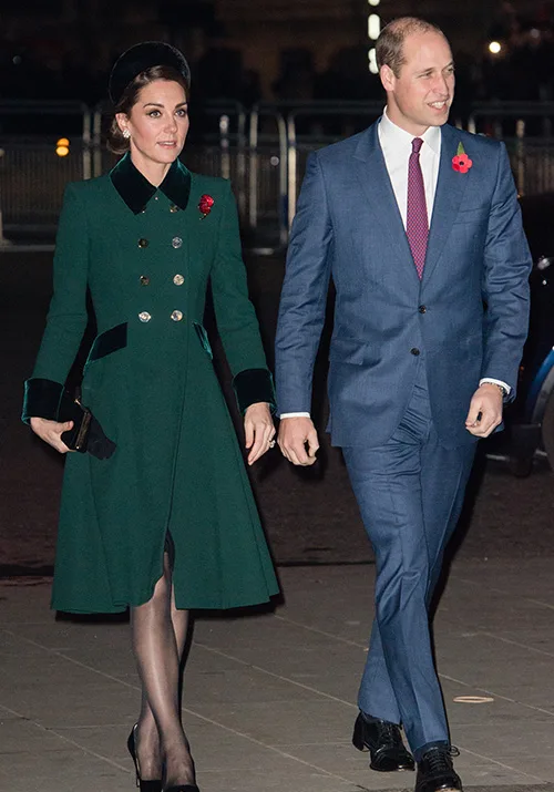 Man in blue suit and woman in green coat walking outside, both wearing poppy pins.