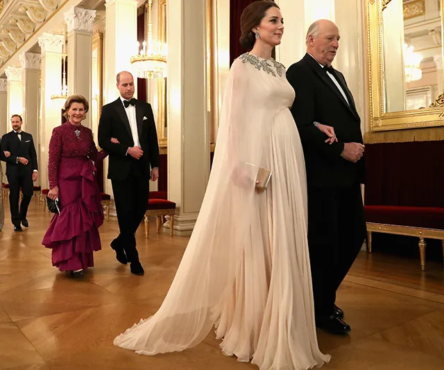 A formal event with elegantly dressed people walking in a lavish hallway.