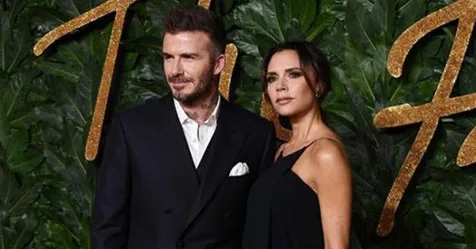 Couple posing at an event with lush greenery and decorative gold lettering in the background.