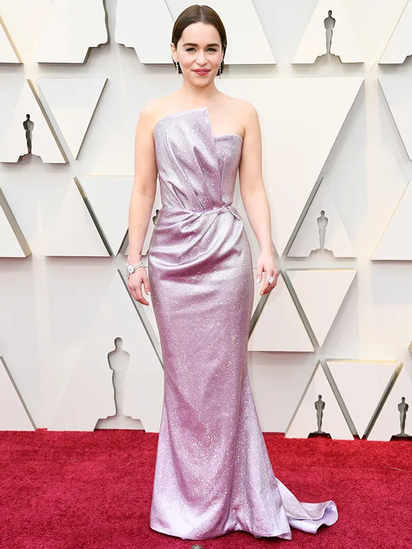 Woman in a shimmering lavender gown poses on a red carpet at an awards event.