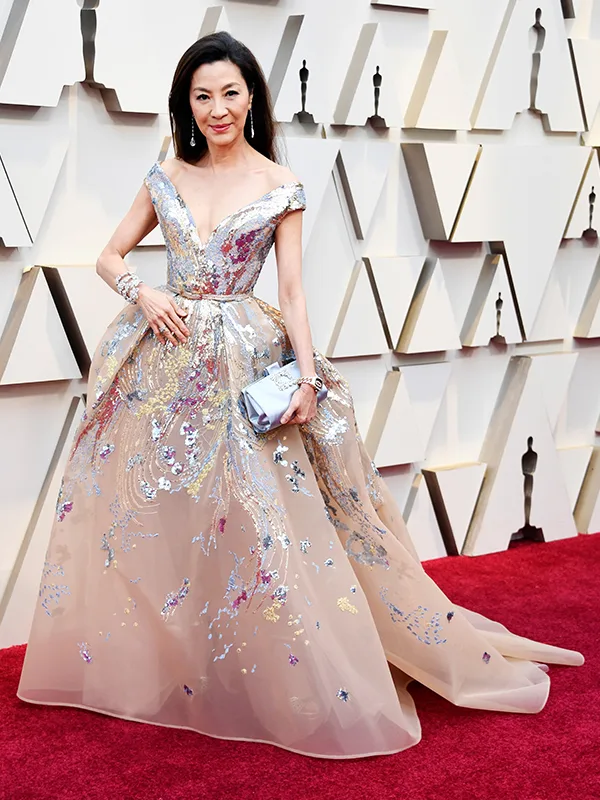 Elegant woman in a floral gown on a red carpet at an event with geometric wall backdrop.