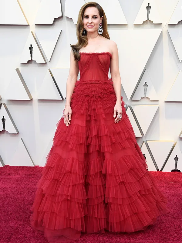 Woman in a strapless red gown on a red carpet, standing against a geometric patterned wall.