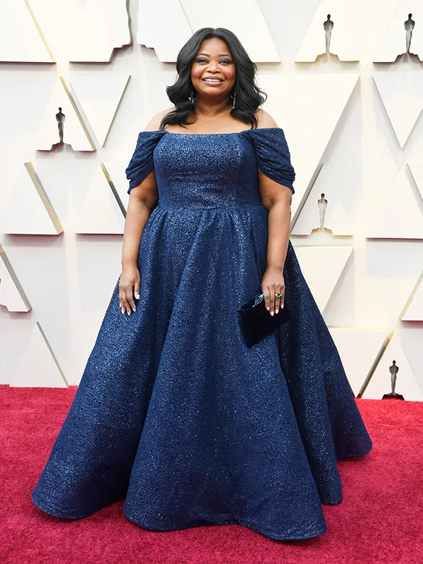 Person in elegant off-shoulder blue gown on red carpet, smiling.