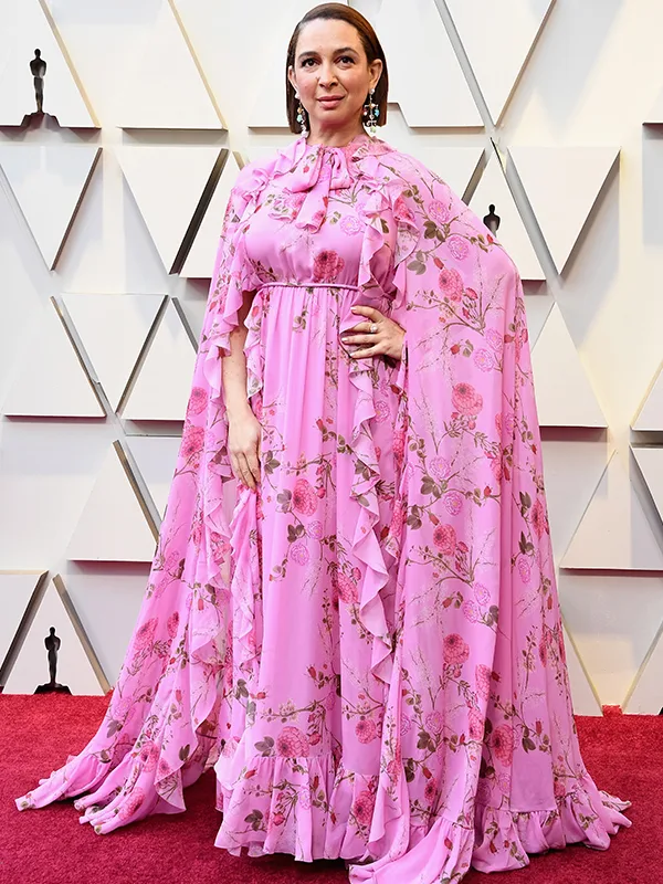 A person in a pink floral gown poses on a red carpet at an awards event.