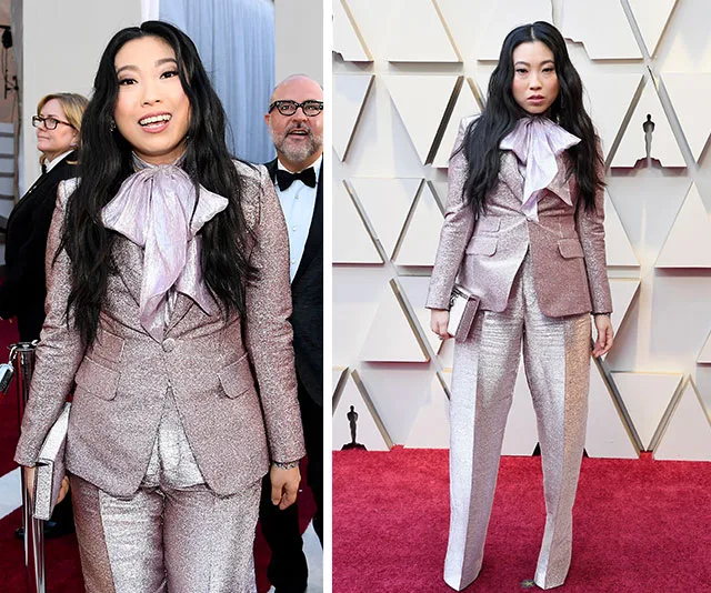 A person in a shiny pink suit and bow tie poses on the red carpet at an award event.