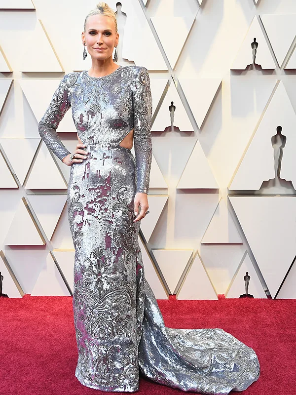 A person in a silver embellished gown poses on a red carpet at an awards event.