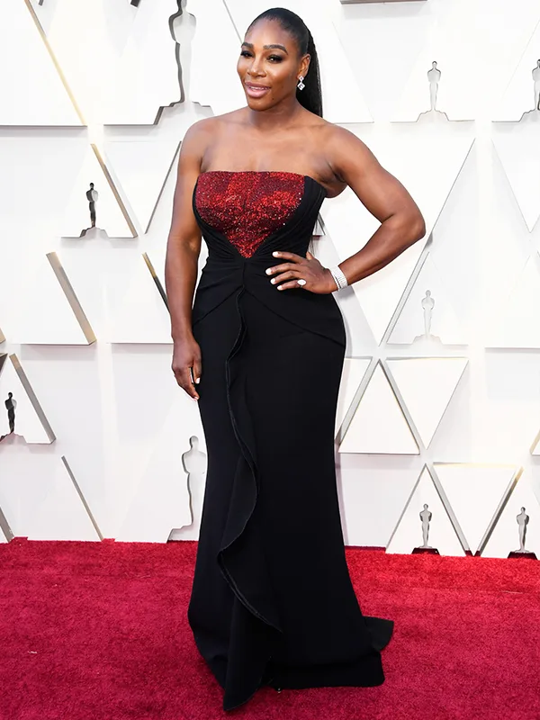 A person in a strapless black and red gown poses on a red carpet at an event.