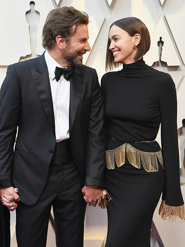 Two people in formal attire holding hands and smiling at each other on a red carpet event.