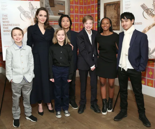 A group of well-dressed people posing together indoors at an event with movie posters in the background.