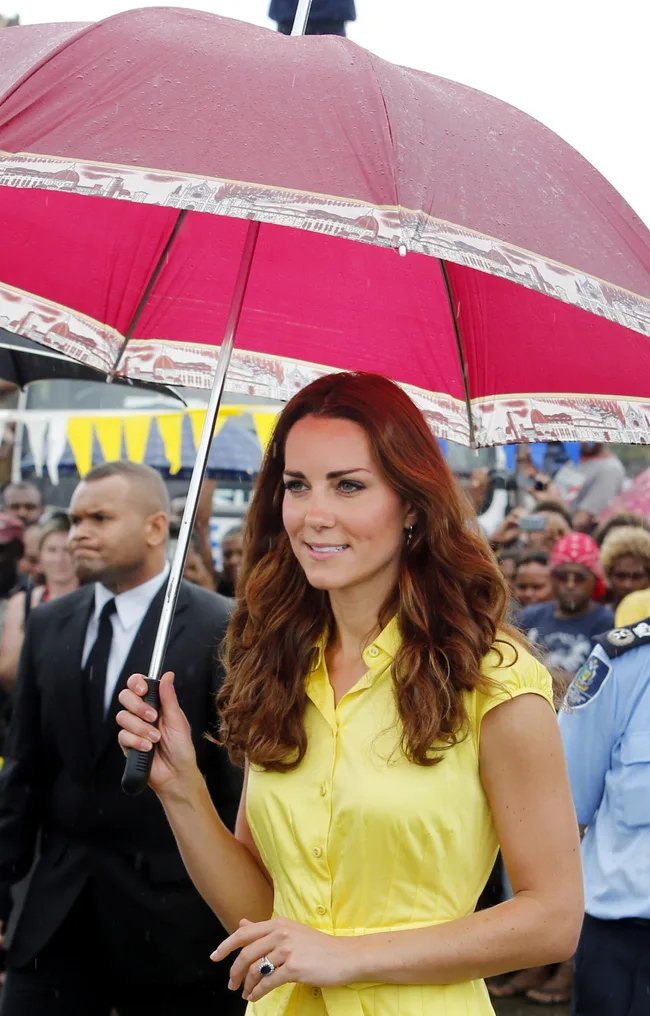 Woman in a yellow dress holding a red umbrella, standing in a crowd on a rainy day.