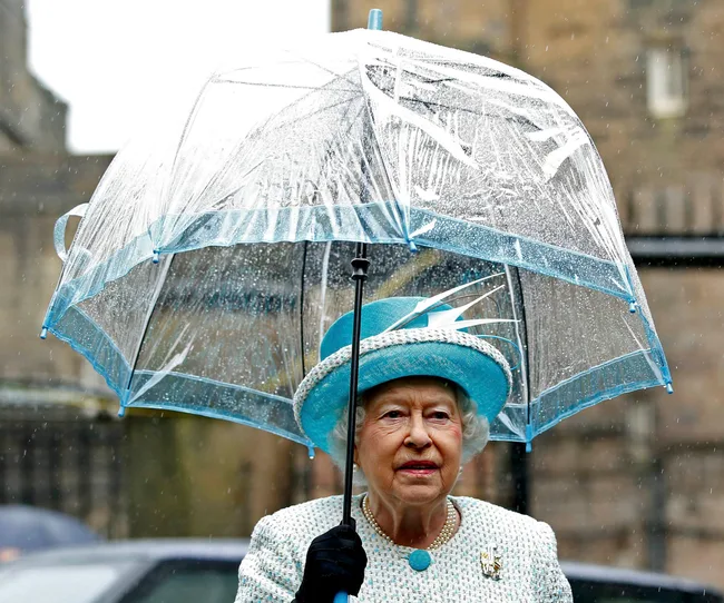 A woman in blue attire holds a transparent umbrella in the rain.