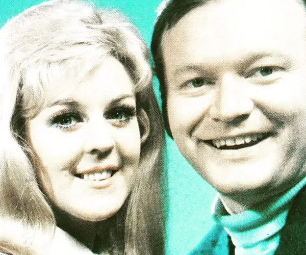 A man and woman smiling at the camera against a green background.