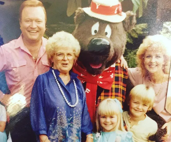 A family poses with a person in a bear costume, including two children and three adults, all smiling.