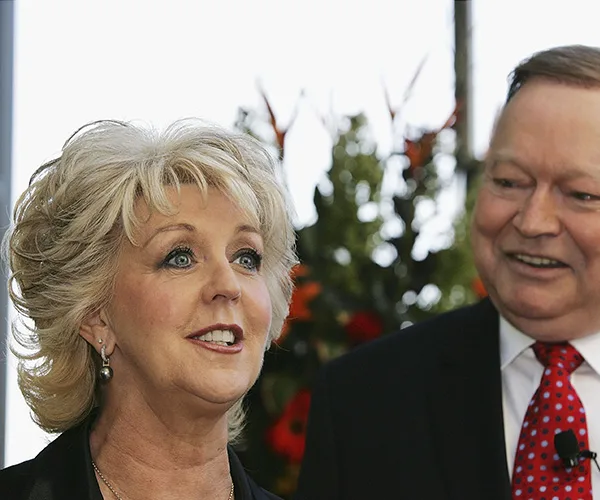 Man and woman smiling in formal attire, with floral background.
