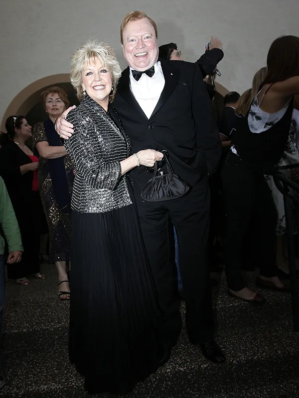 Couple dressed formally, smiling, and posing at an event with a crowd in the background.