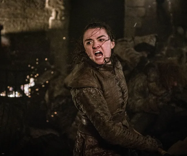 Arya Stark in battle, wearing armor and screaming, with blurred background in "Game of Thrones" scene.