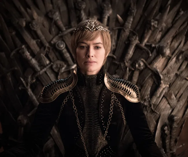 Character in medieval attire sits on a throne made of swords, wearing a crown and looking forward.