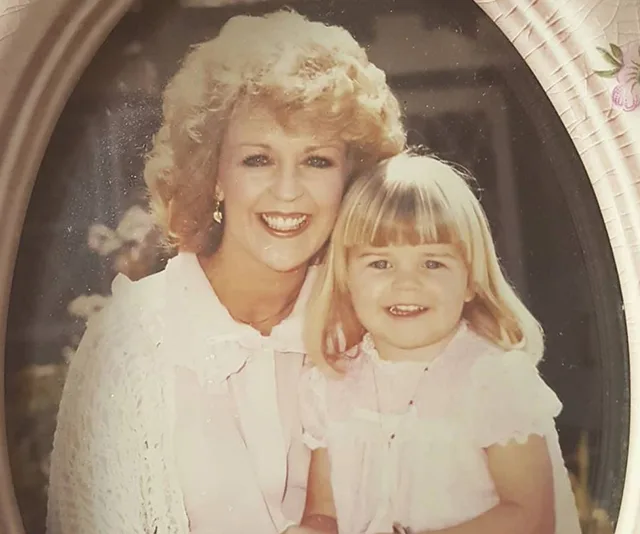 A woman with curly hair and a young girl with bangs smiling in an oval portrait.
