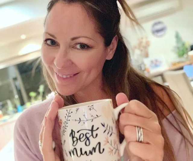 Someone holding a mug that says "Best Mum" with a smile in a cozy indoor setting.