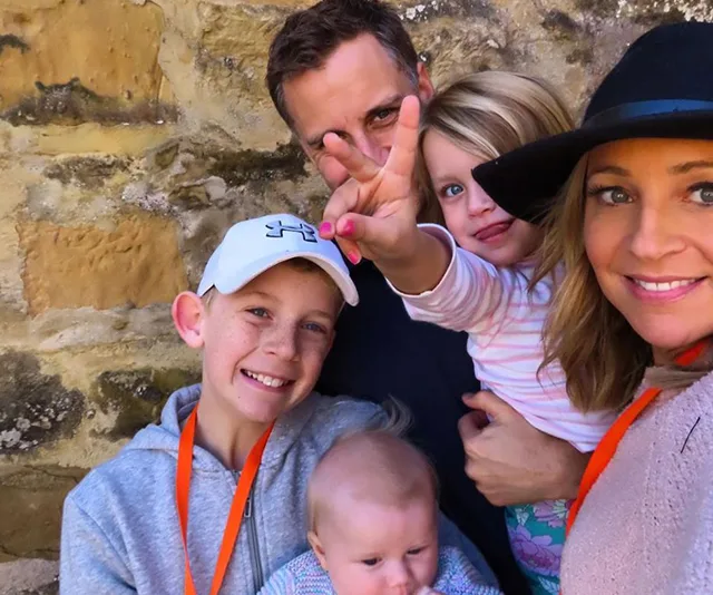 Family of five smiling near a stone wall; one child making a peace sign.