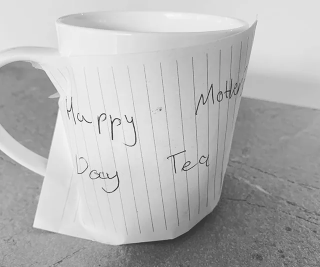 White mug wrapped in lined paper with "Happy Mother's Day Tea" handwritten on it.