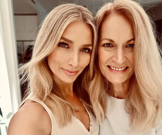 Two women with blonde hair smiling, standing close together indoors.