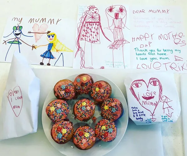 Children's drawings and notes for Mother&rsquo;s Day with decorated cupcakes on a plate.