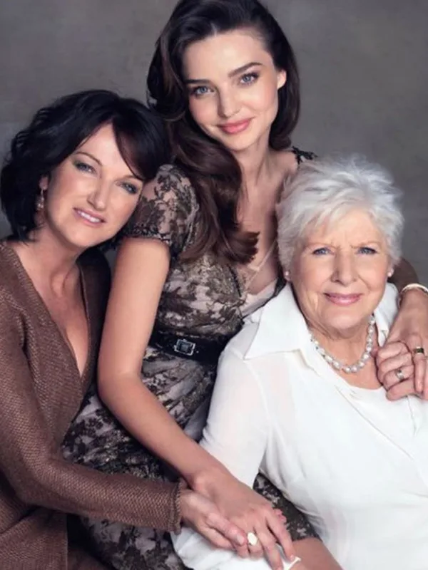 Three women of different generations smiling and sitting close together, with arms lovingly wrapped around each other.