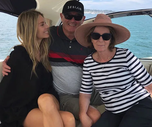 Three people sitting on a boat, smiling. The young woman on the left is wearing a black dress, the older woman a striped shirt and hat.