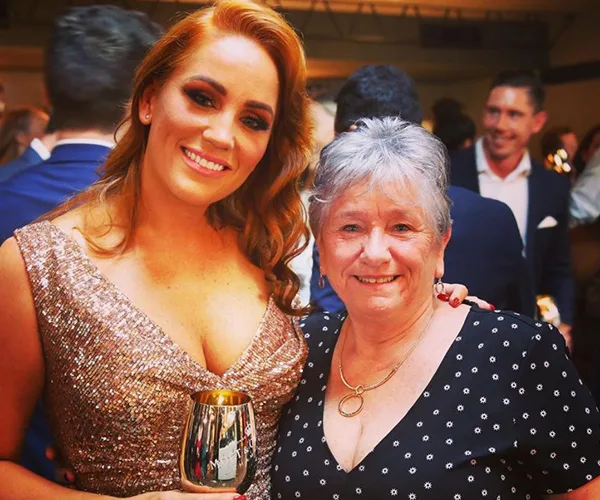 Two women smiling at a party; one in a sparkly dress holding a gold cup, the other in a polka dot top.