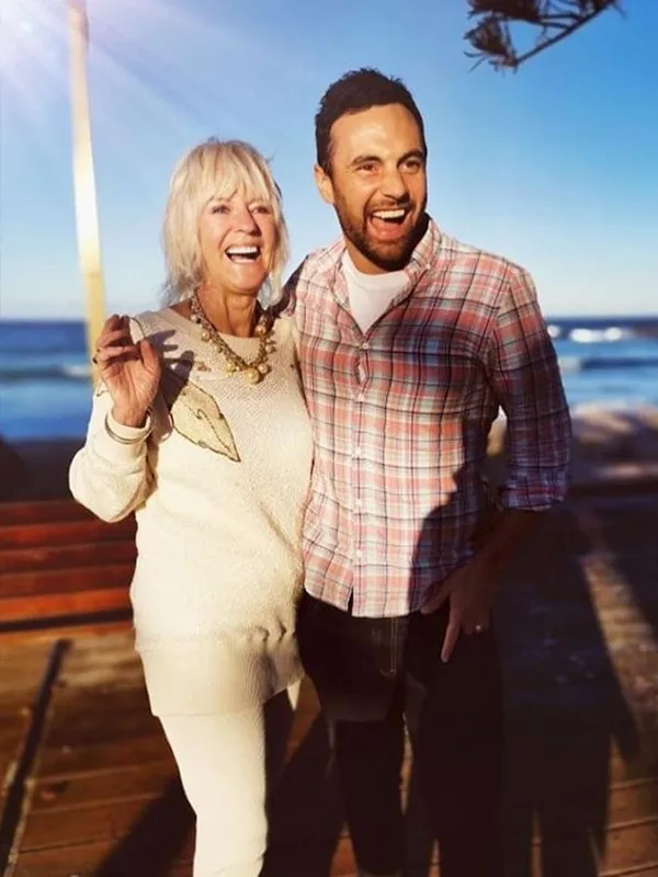 Elderly woman and younger man smiling on a sunny beach boardwalk.