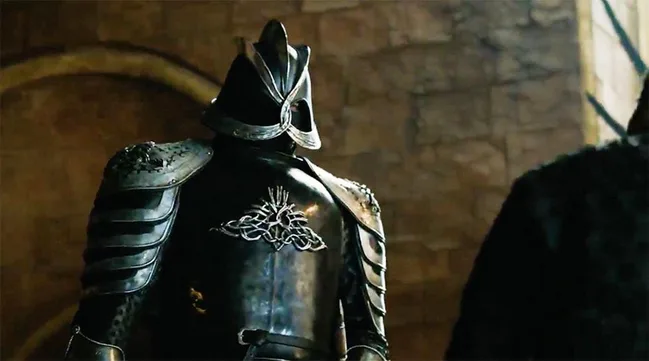 A knight in dark armor with a helmet, standing indoors against a stone backdrop.