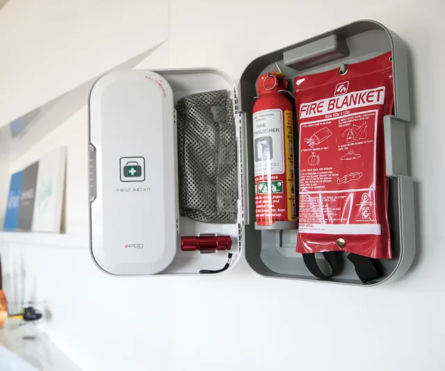 Emergency kit mounted on a wall, including a first aid kit, fire extinguisher, and fire blanket.