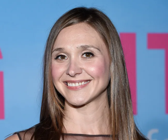 Smiling woman with long brown hair against a blue background.