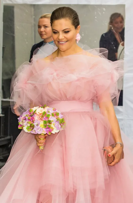 A woman in a pink ruffled gown holding a colorful bouquet, smiling at an event.