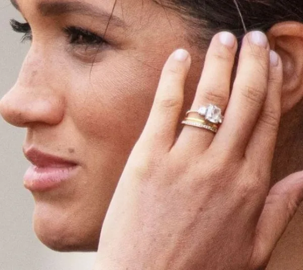 A woman touching her ear, showing a diamond engagement ring and bands on her finger.