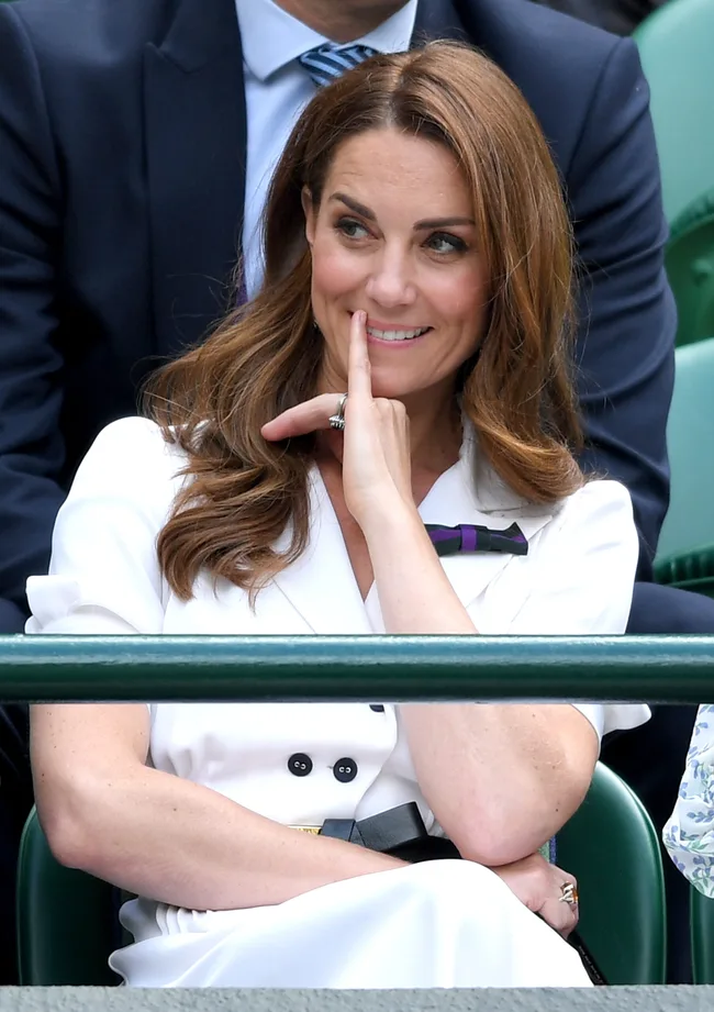 Person in white outfit smiling and sitting at Wimbledon 2019 tennis event.
