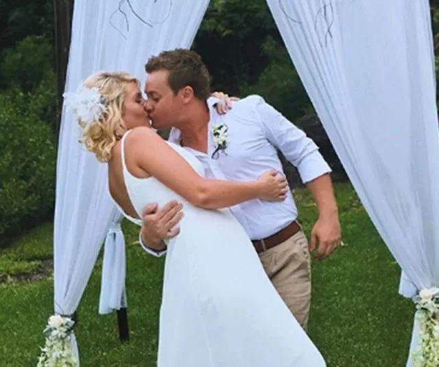Couple kissing under an outdoor wedding arch, surrounded by greenery.