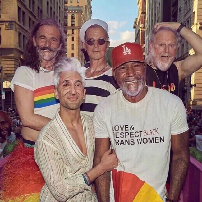 Group photo of diverse individuals at a parade; one wears a "Love & Respect Black Trans Women" T-shirt.