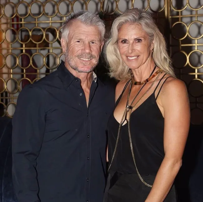 A couple smiling and posing together indoors, with gold circular wall pattern in the background.