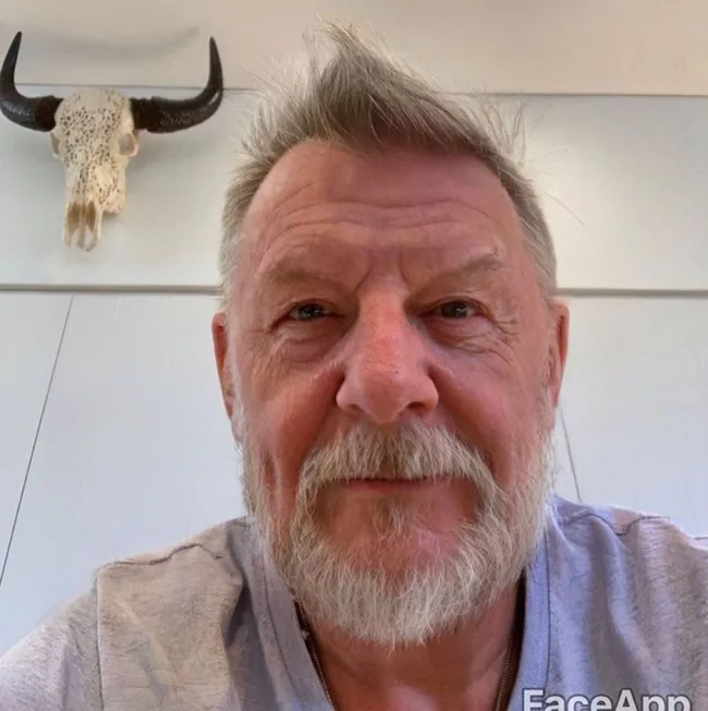 Bearded man with light hair and a buffalo skull mounted on the wall behind him.