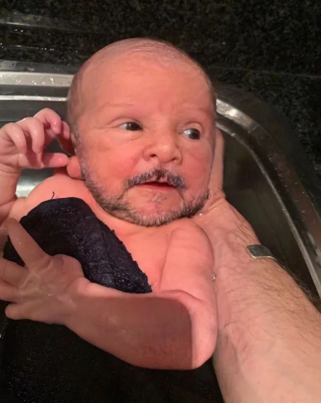 Baby with digitally edited adult face, appearing in a bath, held by an arm.