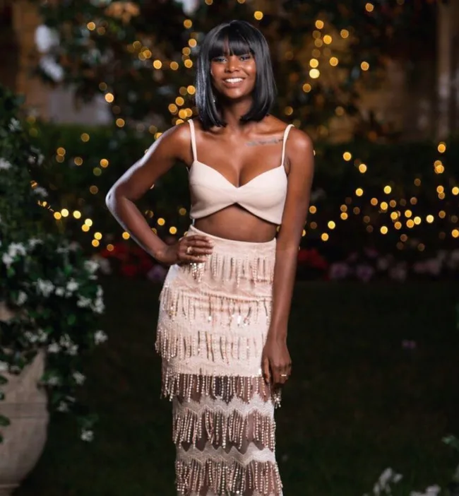 Woman in a stylish outfit with lights in the background, smiling and posing outdoors.