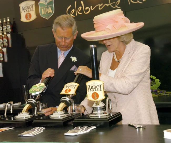 A man and woman pour drinks from Greene King IPA and Abbot Ale taps at a bar, wearing formal attire.