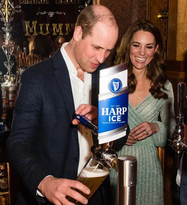 A man pours a pint of beer from a Harp Ice tap, while a smiling woman watches in the background.