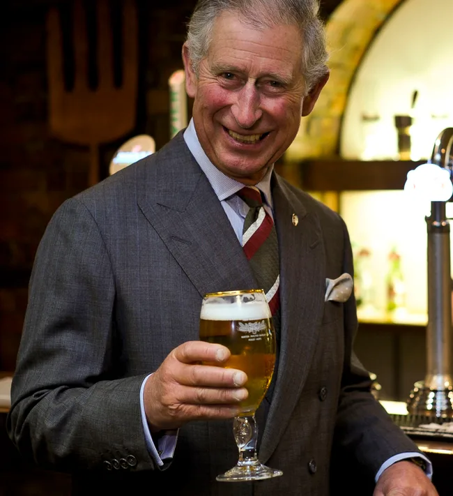 Man in a suit holding a glass of beer and smiling.
